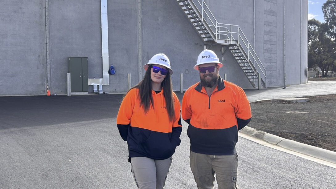 Leed - Teigan Schoots and Leed Project Manager Tasman Scholes wearing hard hats and high vis jumpers are standing in from of the new Shepparton Clear Water Storage Tank